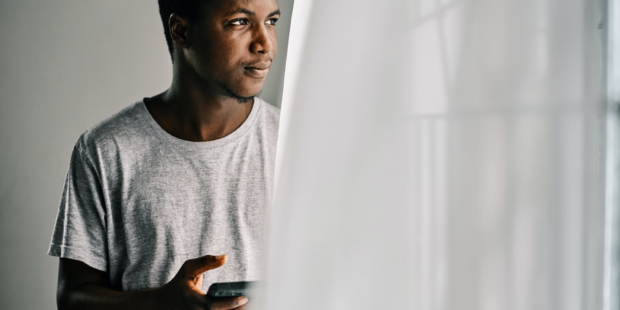 man in gray crew neck shirt holding mobile phone standing beside white curtain - Photo by Emmanuel Ikwuegbu on Unsplash