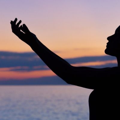 Silhouette of a woman raising her hands against the backdrop of a dusky sky - Photo by William Farlow on Unsplash
