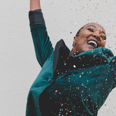 smiling woman in green jacket raising her hands amid shower of confetti - Photo by Clay Banks on Unsplash