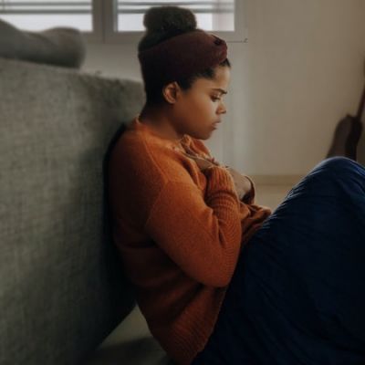 woman with an anxious expression wearing an orange sweater sitting on the floor - Photo by Joice Kelly on Unsplash