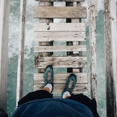 First-person view looking down on a person's shoes, standing on a narrow wooden bridge with turbulent waters below - Photo by Benjamin Davies on Unsplash