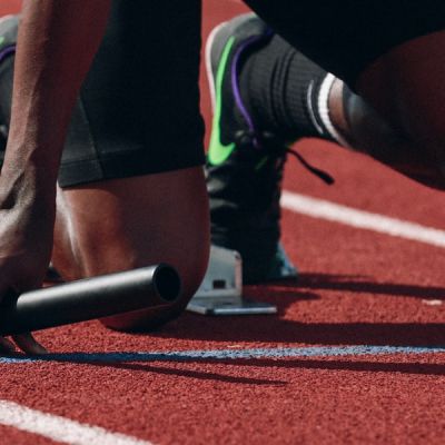 Closeup image of runner crouching in the starting blocks with baton in hand - Photo by Braden Collum on Unsplash